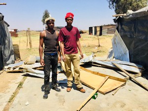 Photo of two men in front of a demolished shack