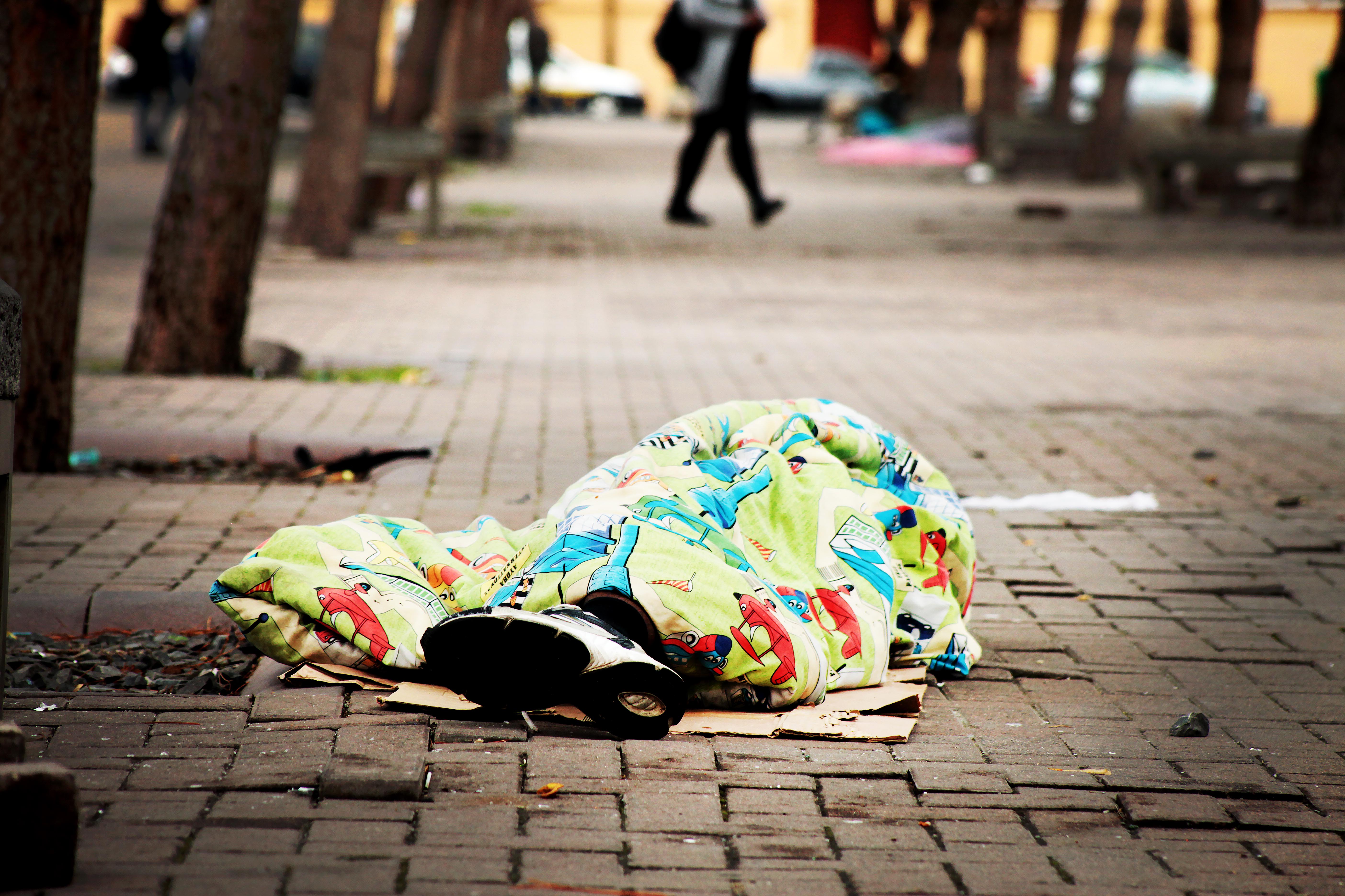 Photo of a man sleeping covered by a blanket on the open street
