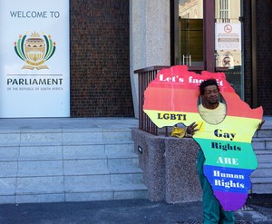 Photo of a man infront of parliament with a gay rights poster